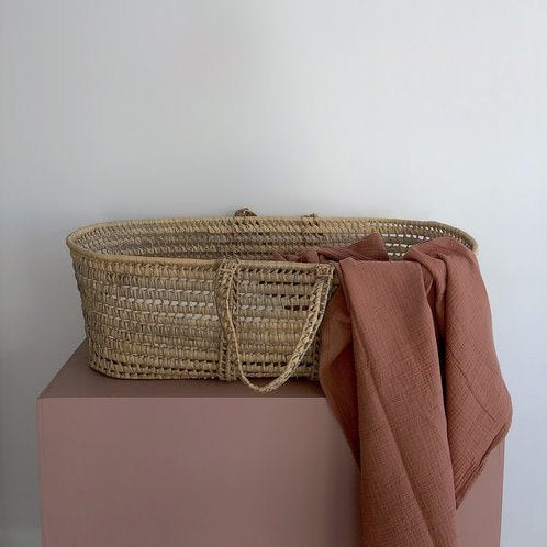 Thursday's Child organic cotton gauze wrap in clay draped on the side of a baby moses basket
