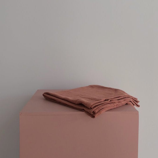 Thursday's Child organic cotton gauze wrap in clay draped on the side of a baby moses basket